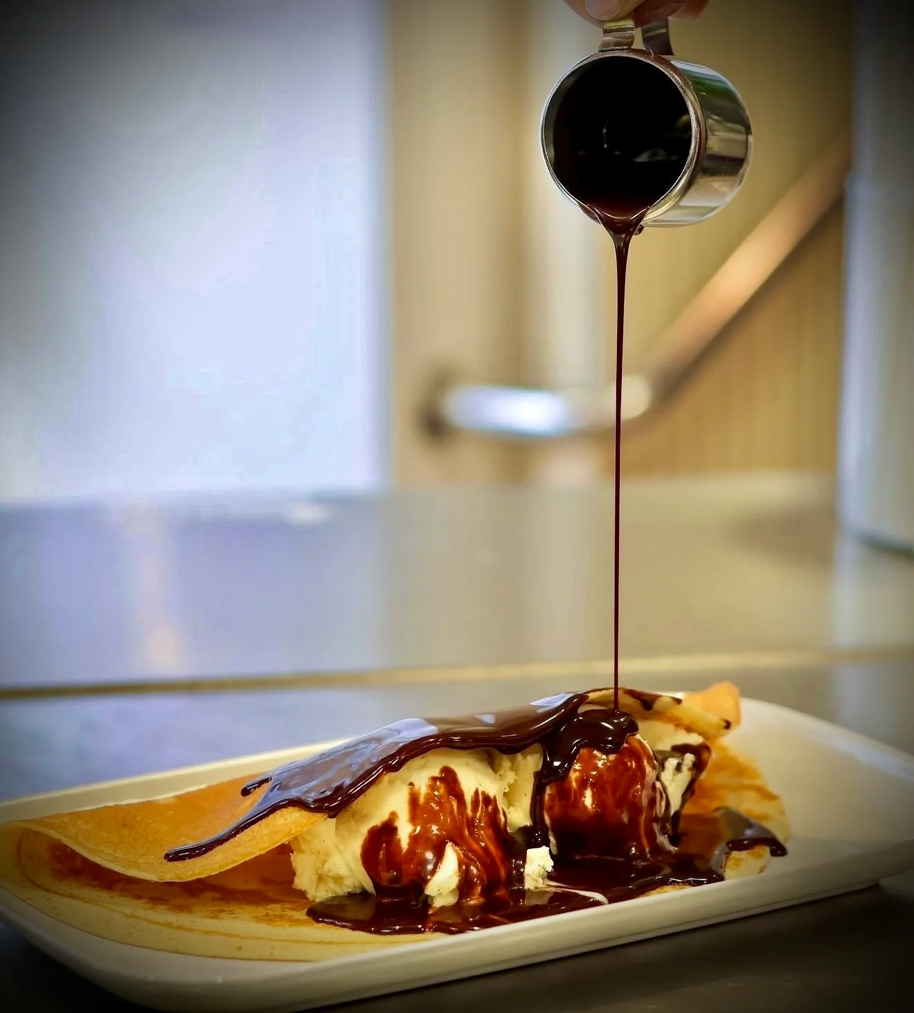 Sauce chocolat versée sur une crêpe accompagnée de glace