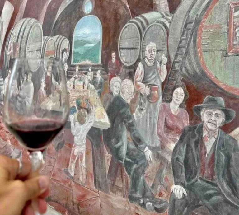 Verre de vin rouge devant une fresque représentant un chai corse